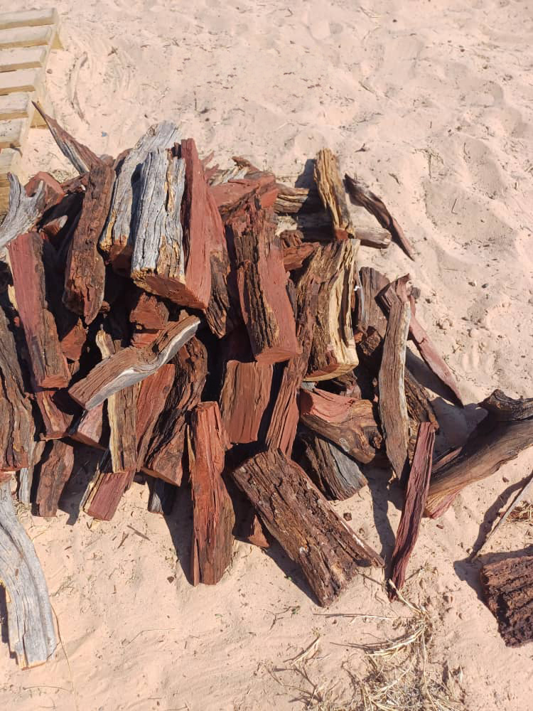 Workers sort a large, reddish-brown pile of sustainably sourced Namibian hardwood firewood, ready for distribution to customers.