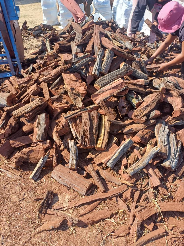 Workers sort a large, reddish-brown pile of sustainably sourced Namibian hardwood firewood, ready for distribution to customers.